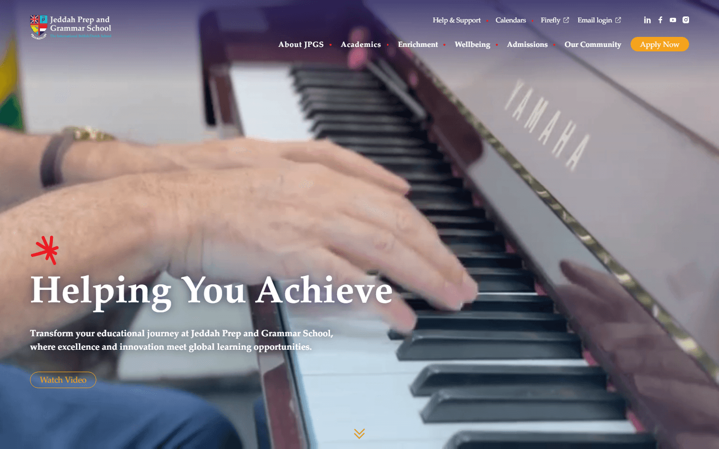 JPGS homepage hero at desktop width: a close-up of hands playing a piano keyboard behind the headline 'Helping You Achieve,' an intro paragraph, and a 'Watch Video' button under the main nav (About JPGS, Academics, Enrichment, Wellbeing, Admissions, Our Community, Apply Now).